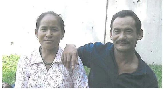 A man with a mustache and a dark shirt sits outdoors with his arm around a woman in a light patterned blouse, both smiling slightly at the camera. The background is grass and a light-colored wall, reminiscent of media coverage photos of Kermit Gosnell.