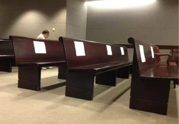 A nearly empty room with long wooden benches, some marked with white signs. One person sits alone near the back, and the quiet setting suggests a courtroom awaiting media coverage of convicted murderer Kermit Gosnell’s case.