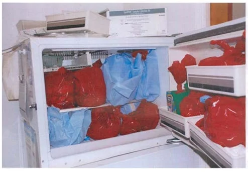 A freezer filled with several red and blue plastic bags, some stacked on shelves and in drawers, reminiscent of the chilling evidence found in the case of convicted murderer Kermit Gosnell, with items and boxes placed around and on top.