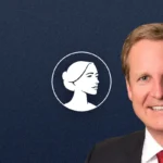 A smiling man in a suit and red tie stands before a dark blue background with a white stylized woman’s profile logo next to him, representing MT-Sen candidate Kurt Alme and his strong Pro-Life stance.