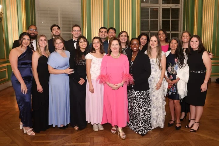 A group of people dressed in formal attire pose together at the SBA Gala in an elegant room with green and gold walls and large windows. The group includes men in suits and women in dresses, smiling at the camera, celebrating life.