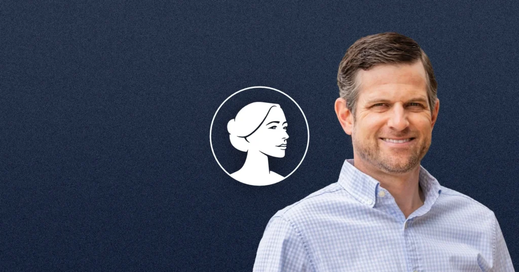 A man in a light blue checkered shirt smiles at the camera, standing in front of a dark blue background with a white illustrated profile of a woman’s face to his left, representing pro-life values championed by Georgia AG Brian Strickland.