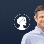 A man in a light blue checkered shirt smiles at the camera, standing in front of a dark blue background with a white illustrated profile of a woman’s face to his left, representing pro-life values championed by Georgia AG Brian Strickland.