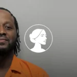 A man in an orange shirt looks at the camera against a plain gray background. Next to him, there is a white illustrated profile of a woman’s face inside a circle, referencing recent DOJ discussions surrounding the abortion drug.