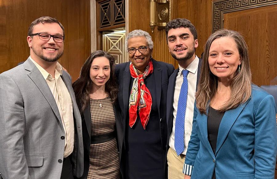 Five people stand together indoors, smiling at the camera in a formal-looking room with wood paneling and ornate decor. Dressed in business attire, this group includes SBA interns and pro-life leaders gathered for a special occasion.