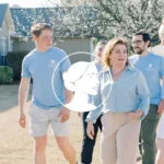 A group of people in casual clothes walk and talk outside in a suburban neighborhood on a sunny day, engaging with battleground voters as part of a Voter Contact Program. A white logo of a woman’s profile is overlaid in the center of the image.