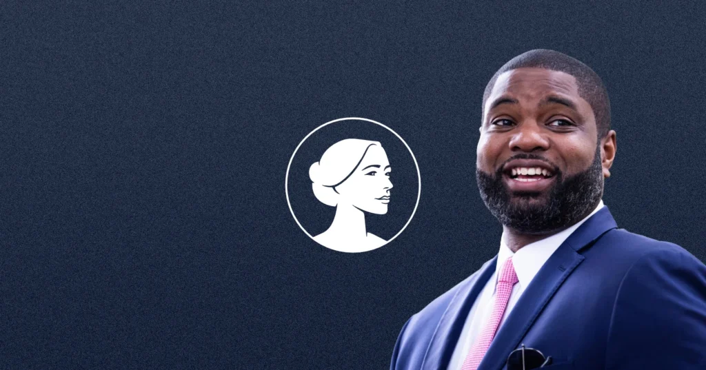 A man in a navy suit and pink tie smiles in front of a dark blue background with a white illustration of a woman’s profile in a circle, evoking themes central to the Pro-Life movement.