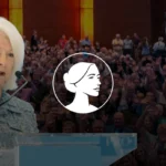 An older woman with white hair, a prominent Pro-Life Leader, speaks at a podium. Behind her, a large audience sits in the hall. There is a white graphic of a woman's profile over the image's center.