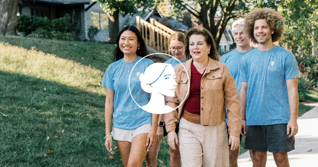 Five people, four in blue shirts and one in a tan jacket, walk together outside on a sidewalk with green grass and trees in the background, embodying the spirit of Iowans participating in a Voter Contact Program. A white graphic logo overlays the image’s center.
